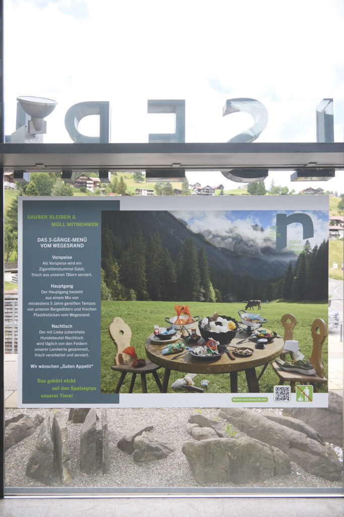 Sauber Bleiben und Muell Mitnehmen campaign poster with alpine sky reflected in the glass, Walserhaus