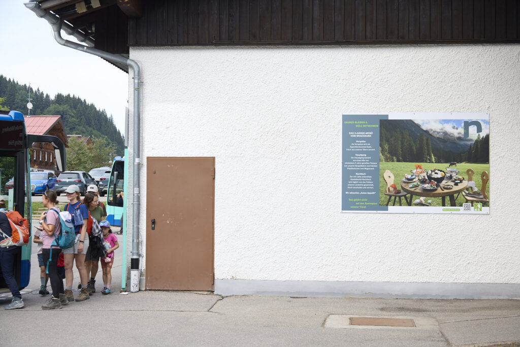 Sauber Bleiben campaign billboard on a house wall with hikers passing, Kleinwalsertal