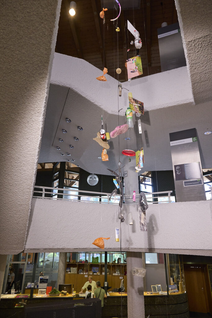 Trash mobile of collected litter cascading through the Walserhaus atrium, Naturbewusst Erleben campaign by Mathias Kessler