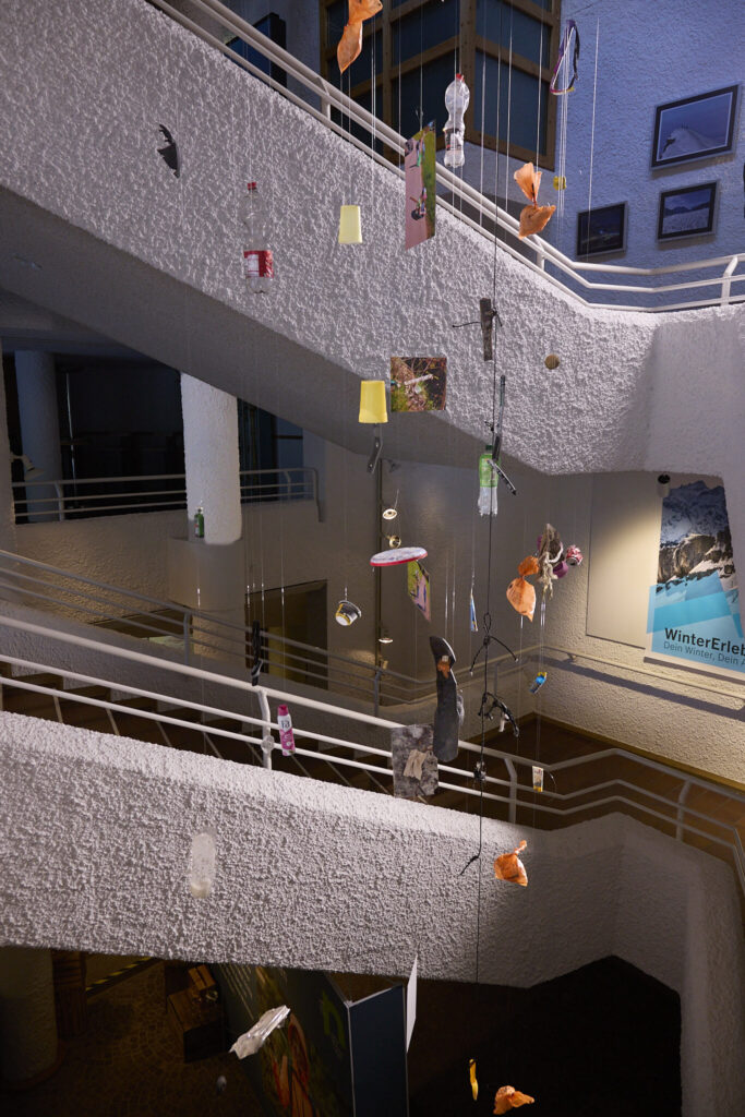 Trash mobile installation hanging across the staircases of the Walserhaus at dusk, Sauber Bleiben campaign Kleinwalsertal