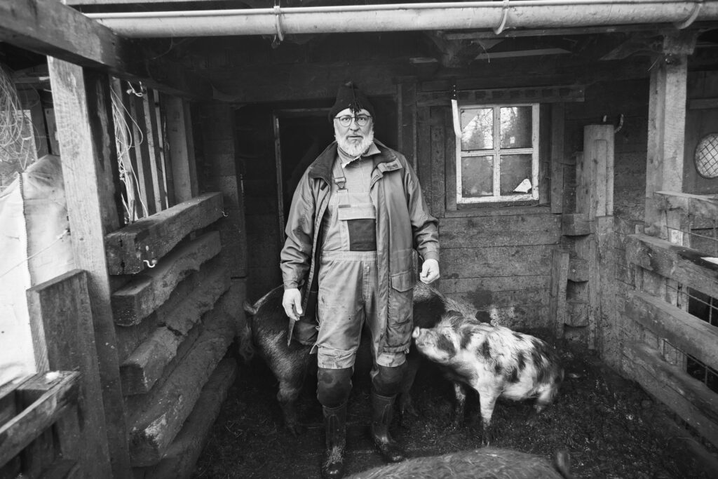 Jeremias Kessler with his pigs in the barn, black-and-white environmental portrait by Mathias Kessler
