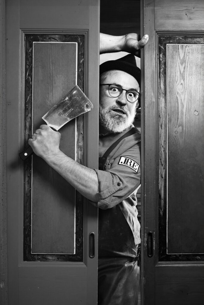 Jeremias Riezler peering through a door with a meat cleaver, black-and-white portrait by Mathias Kessler